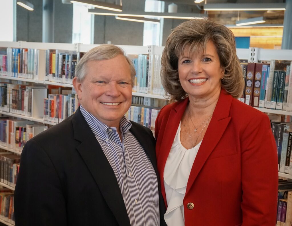 Photo of Rick and Denise Mills smiling while surrounded by books in the Johnson County Library.