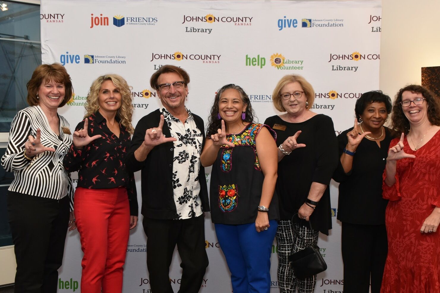 Group of library lovers attending the Library Lets Loose event, smiling and holding up fingers in the shape of an L.